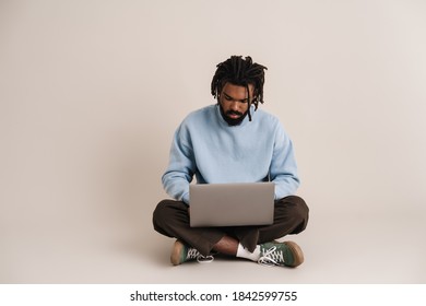 Serious african american guy working with laptop while sitting on floor isolated over white background - Powered by Shutterstock