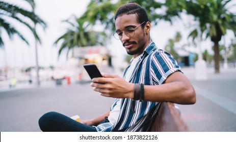 Serious African American Hipster Guy Recreating On Bench Holding Mobile Phone For Watching Videos, Pensive Dark Skinned Man Generation Z Checking Notification About Mail And Messages Outdoors