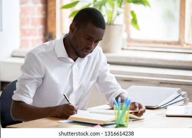 Serious African American Man University Student Studying Reading Textbook Making Notes, Focused Black Guy Doing Literature Research Assignment Learning With Book Writing Essay Sitting At Desk