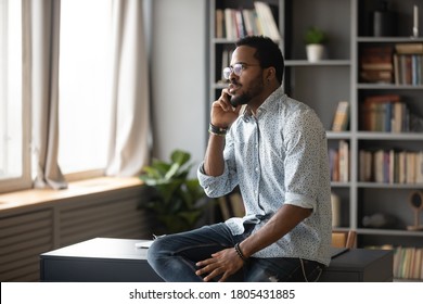 Serious African American Man Wearing Glasses Talking On Phone, Making Call, Sitting On Work Desk, Confident Businessman Consulting Client Customer By Cellphone, Negotiating With Partners