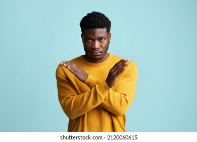 Serious african american millennial guy in casual saying no, looking at camera and showing hands crossed over chest, blue studio background, copy space. Human gestures concept