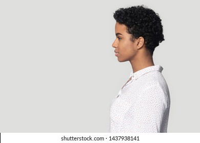 Serious african American millennial woman stand in profile view isolated on grey studio background look at blank copy space aside, focused black girl stare at free copyspace, ad sale offer place