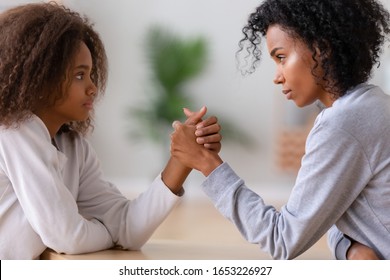 Serious African American Mom Nanny And Teen Daughter Arm Wrestling Looking In Eyes Fighting, Angry Black Mother And Teenage Girl Holding Hands Competing, Family Parent Children Disagreement Concept