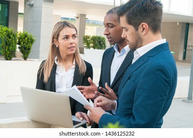 Serious African American team leader explaining project details to colleagues. Men and woman in office suits standing outdoors, using laptop and talking. Teamwork concept - Shutterstock ID 1436125232