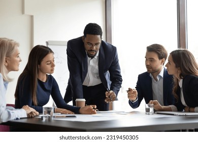 Serious African American team leader talking to employees, discussing project, reviewing sales result on corporate meeting. Business coach, teacher training group of interns, explaining documents - Powered by Shutterstock