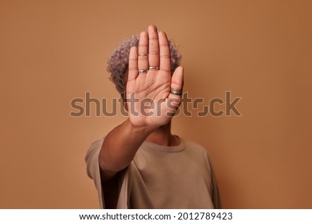 Serious African American woman covers herself with her palm, confidently shows prohibitory gesture stop and no signs shakes her head. Young ethnic woman against violence defends personal boundaries.