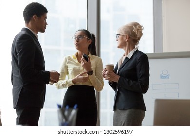 Serious African Asian And Caucasian Colleagues Talking At Work Break Discussing New Ideas In Office, Diverse Team People Having Business Conversation Standing Together After Training Conference