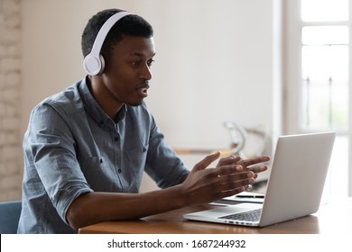 Serious african businessman wearing wireless headphones makes conference video call talk looks at pc screen, student and e-learning, salesman support agent helpline representative on-line chat concept