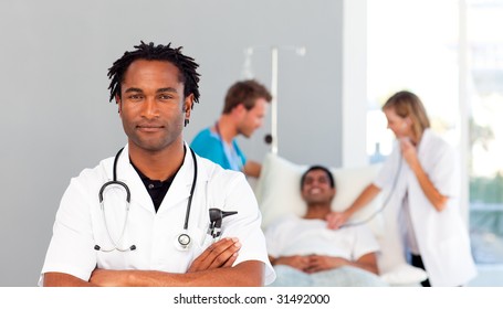 Serious African Doctor With Folded Arms And Patient In The Background