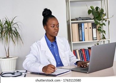 Serious African Female Doctor Watching Online Medical Webinar Seminar Training Elearning On Laptop Make Notes. Black Woman Physician Gp Participate Video Conference Call Videoconferencing On Computer.