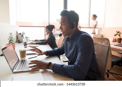 Serious african male call center telesales agent wear wireless headset talk consult online client use computer, black operator telemarketer work in customer service helpline support office with team