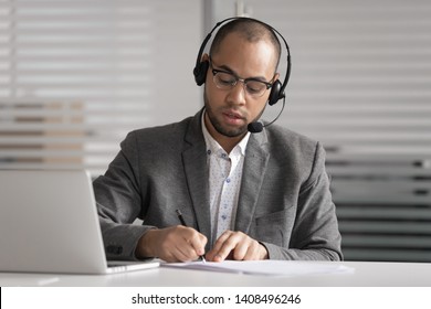 Serious African Male Customer Support Service Agent Wear Wireless Headset Talk Write Notes Make Video Conference Call, Focused Mixed Race Businessman Operator Representative  Online Chat