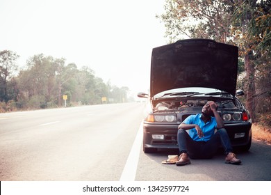 Serious African Man Holding His Head By Hands Standing Near His Old Broken Car  With Raised Hood On The Highway Road