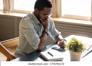 Serious African man read message on smart phone he looks focused or worried by received news, businessman sitting at workplace desk use cellphone websurfing or learn new e-business application concept - Shutterstock ID 1755781172