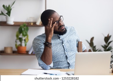 Serious african millennial businessman thinking cogitating about business issues. Frustrated black entrepreneur searching problem solution sitting alone on chair at modern office desk looking away - Shutterstock ID 1253228182