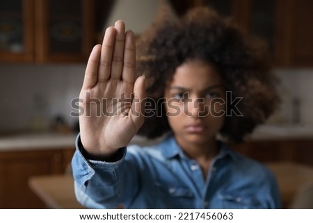 Serious African teenager girl looking at camera raises her palm showing stop gesture, against emotional and physical abuse, bullying at school, racial inequality, struggling for women rights, close up
