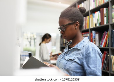 Serious African woman wearing eyeglasses examining the book she searching for the book in the library - Shutterstock ID 1578126559