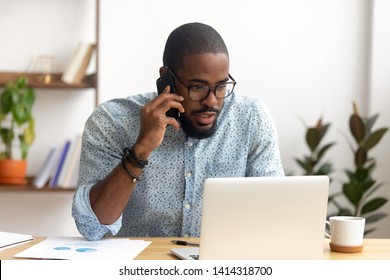 Serious african-american employee making business call focused on laptop at workplace. Black businessman consulting customer, discussing financial report. Contract negotiation and discussion concept - Shutterstock ID 1414318700