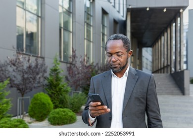 Serious afro american boss in business suit walking outside office building, mature man holding phone, businessman concentrating reading message and typing text. - Powered by Shutterstock