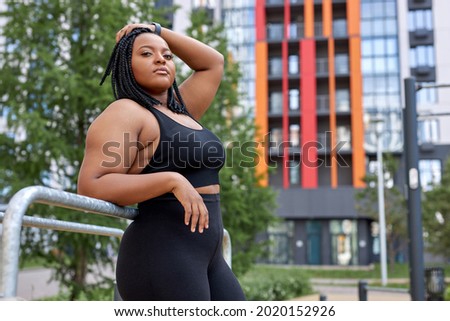 Serious Afro American Lady Posing Looking At Camera Outdoors, In Sportive Clothes, In Sports Ground, Weight Loss And Fitness Concept. Beautiful Woman Plus Size Model. In Citym Training On Fresh Air