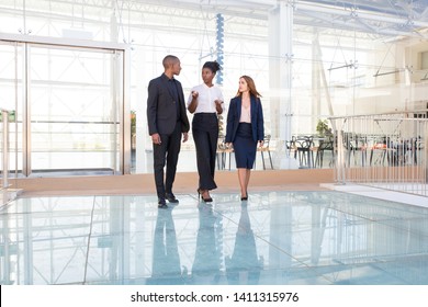 Serious Afro American Manager Telling Investors About Project. Three Mix Raced People In Formal Suits Walking Through Office Hall And Talking. Meeting Or Negotiation Concept