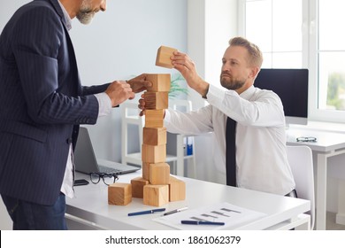 Serious aged father and young son making wood block tower on office desk as metaphor of building family business, enterprise succession, risk management, support and maintaining financial stability