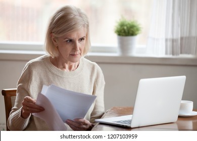 Serious Aged Woman Holding Documents, Checking Information At Laptop Online, Concerned Senior Female Managing Bank Insurance Or Loan Papers, Busy Working At Computer. Elderly And Technology Concept