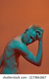 Serious Albino Caucasian Guy Touching His Head And Looking At Camera. Young Modern Bearded Blonde Man Of Generation Z With Naked Torso. Isolated On Orange Background. Studio Shoot. Copy Space