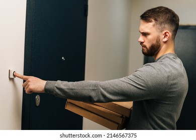 Serious angry delivery man holding in hand carton boxes with hot pizza and ringing doorbell of customer apartment. Side view of courier male delivering online fast-food order, rings bell doorstep.