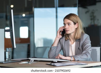 Serious And Anxious Business Woman Talking On The Phone, Working In A Modern Office At The Computer, Close-up Photo Of A Business Conversation