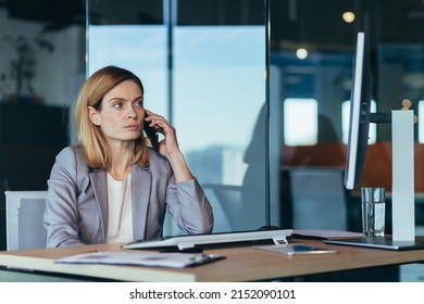 Serious And Anxious Business Woman Talking On The Phone, Working In A Modern Office At The Computer, Close-up Photo Of A Business Conversation