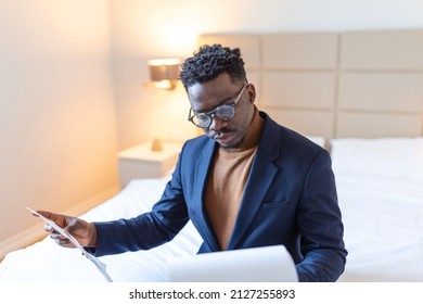 Serious Arican business man sitting on hotel bed working, analyzes expenses on business trip at the hotel room. - Shutterstock ID 2127255893