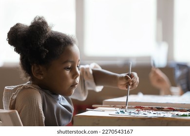 Serious artistic school African American pupil girl painting on canvas on group class, mixing paints on palette with paintbrush, studying creativity, working at table in studio - Powered by Shutterstock