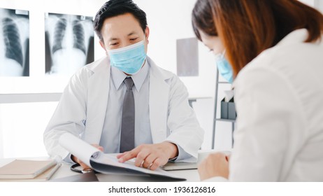 Serious Asia Male Doctor Wear Protective Mask Using Clipboard Is Delivering Great News Talk Discuss Results Or Symptoms With Female Patient In Hospital Office. Lifestyle New Normal After Corona Virus.