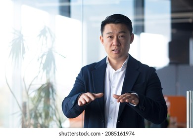 Serious Asian Boss Businessman Looks At The Camera Holds An Online Meeting, Gestures With His Hands A Man Explains The Task To Colleagues