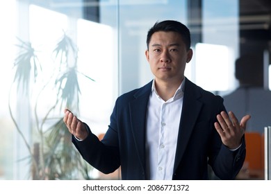 Serious Asian Boss Businessman Looks At The Camera Holds An Online Meeting, Gestures With His Hands A Man Explains The Task To Colleagues