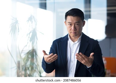 Serious Asian Boss Businessman Looks At The Camera Holds An Online Meeting, Gestures With His Hands A Man Explains The Task To Colleagues