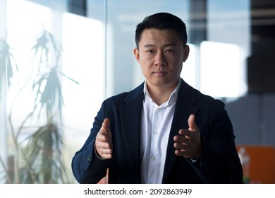 Serious Asian Boss Businessman Looks At The Camera Holds An Online Meeting, Gestures With His Hands A Man Explains The Task To Colleagues