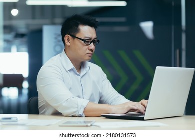 Serious Asian Boss In Glasses Working And Typing On Laptop, Man Concentrated In Modern Office