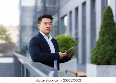 Serious Asian Boss Reads News From Tablet Near Modern Office Male Businessman In Business Suit