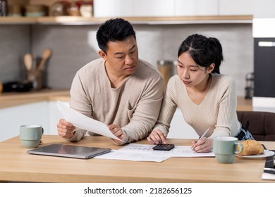 Serious Asian Family Husband And Wife Sitting At Kitchen Table Full Of Papers, Laptop, Coffee Mugs, Counting Monthly Expenses, Using Calculator, Short Of Money. Economy, Family Budget Concept