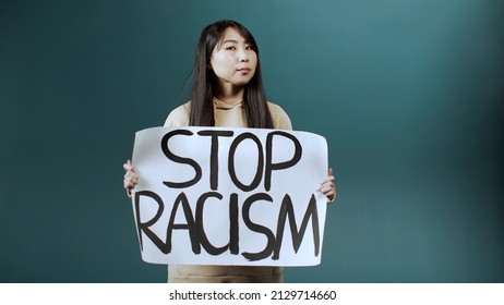 A Serious Asian Lady Is Standing And Raising Up A Poster Against Racism