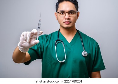 Serious Asian Male Doctor Wearing Rubber Gloves And Scrubs, Looking Amazed At Syringe With Vaccine, Isolated Over White Background