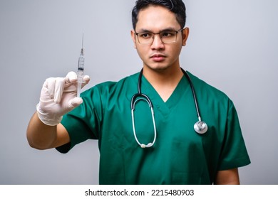 Serious Asian Male Doctor Wearing Rubber Gloves And Scrubs, Looking Amazed At Syringe With Vaccine, Isolated Over White Background