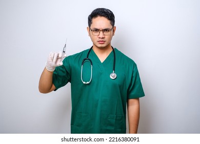 Serious Asian Male Doctor Wearing Rubber Gloves And Scrubs, Looking Amazed At Syringe With Vaccine, Isolated Over White Background