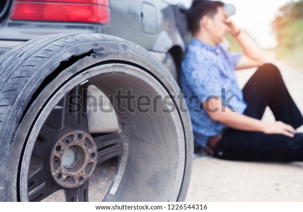 Serious asian man are sitting with headache\
because the wheel of car\
broken.