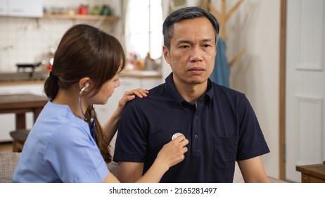 Serious Asian Mature Man Staying Silent While Nursing Aide Is Examining His Breathing With Stethoscope At Home. In-home Social Healthcare For Senior People Concept