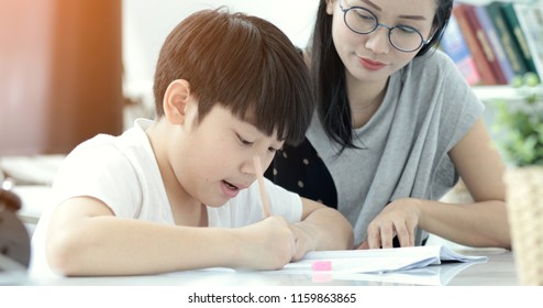 Serious Asian Mother With Son Doing Homework In The Living Room. Mom Teaches Son How To Genius.