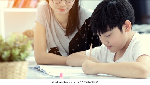 Serious Asian Mother With Son Doing Homework In The Living Room. Mom Teaches Son How To Genius.