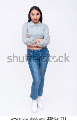 A serious asian woman with mid-length straight hair in a long sleeved cutoff blouse and blue jeans. Possible college student. Isolated on a white backdrop.